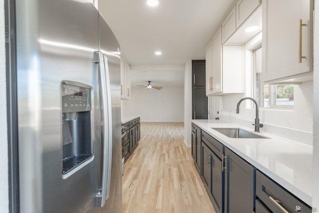 kitchen with stainless steel fridge, light wood-type flooring, light stone counters, sink, and white cabinetry