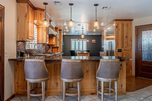 kitchen with a kitchen breakfast bar, dark stone countertops, kitchen peninsula, and hanging light fixtures