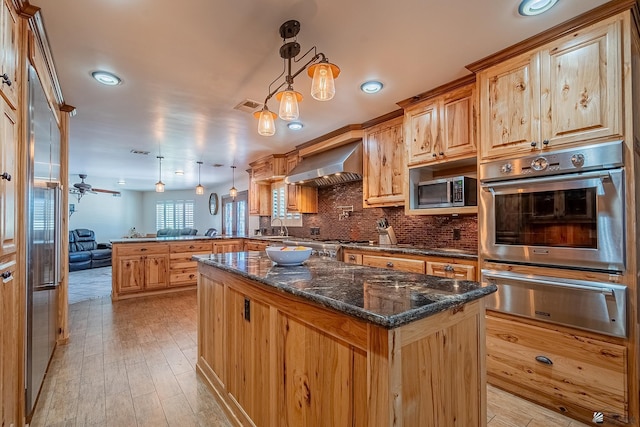 kitchen with wall chimney range hood, tasteful backsplash, a center island, and decorative light fixtures