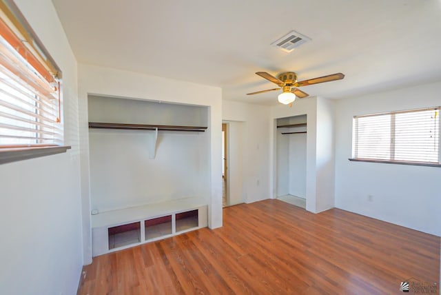 unfurnished bedroom featuring wood finished floors, visible vents, ceiling fan, and two closets