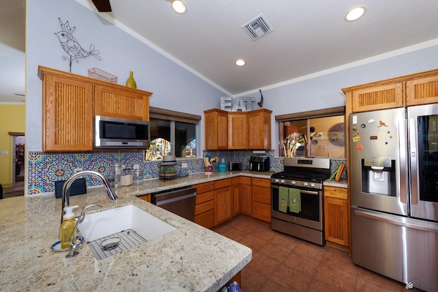 kitchen featuring light stone counters, lofted ceiling, appliances with stainless steel finishes, and sink