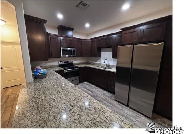 kitchen featuring appliances with stainless steel finishes, sink, light stone countertops, dark brown cabinets, and light wood-type flooring