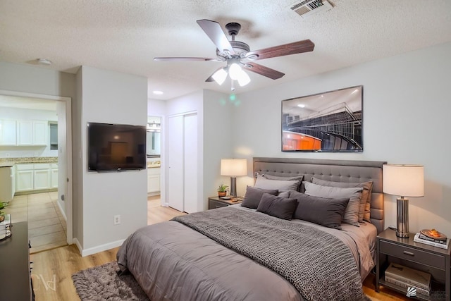 bedroom featuring ensuite bathroom, ceiling fan, light wood-type flooring, and a textured ceiling