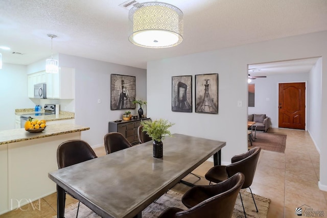 dining space featuring ceiling fan, light tile patterned flooring, and a textured ceiling