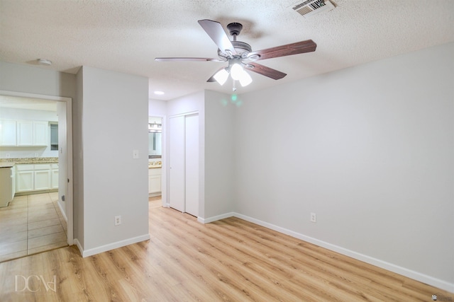 empty room with ceiling fan, light hardwood / wood-style floors, and a textured ceiling