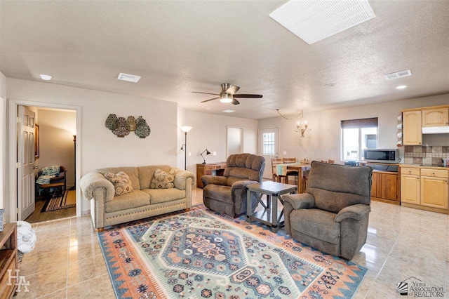 tiled living room with a textured ceiling and ceiling fan with notable chandelier