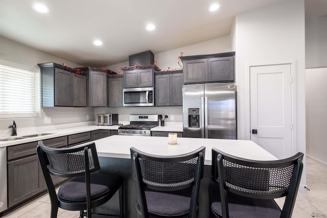 kitchen featuring a center island, stainless steel appliances, light countertops, a sink, and a kitchen bar