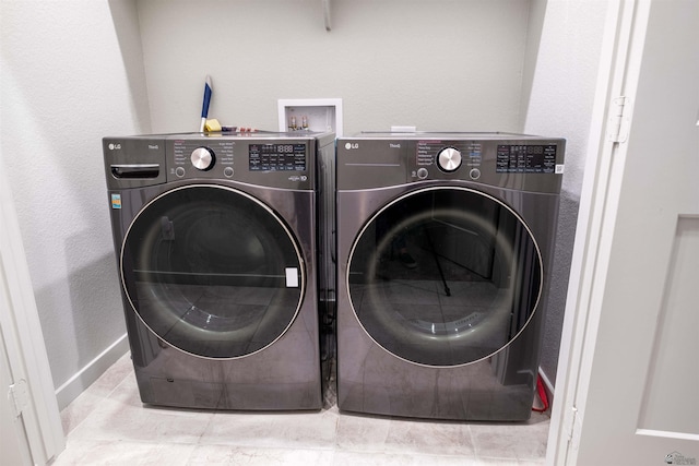 clothes washing area featuring washing machine and dryer, tile patterned flooring, and baseboards