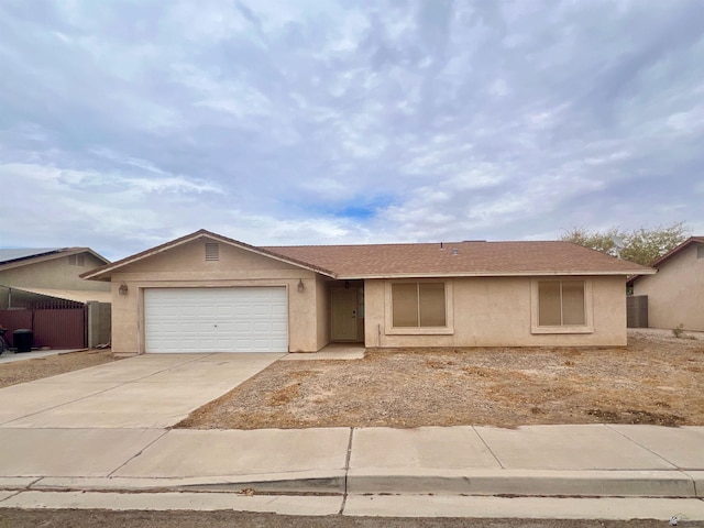 ranch-style home with a garage, concrete driveway, fence, and stucco siding