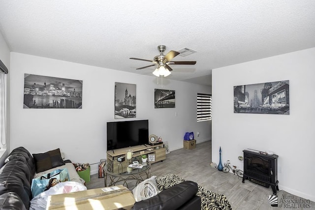 living area with a textured ceiling, wood finished floors, visible vents, a ceiling fan, and a wood stove