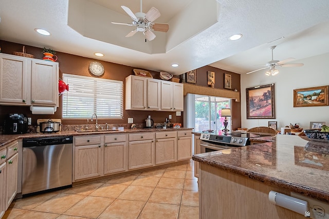 kitchen with appliances with stainless steel finishes, a tray ceiling, sink, light tile patterned flooring, and light brown cabinets