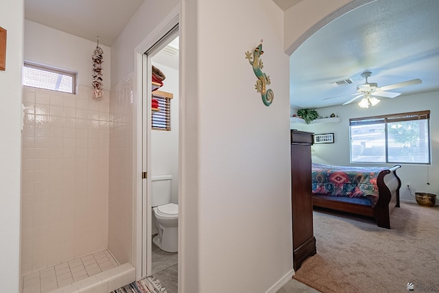 bathroom with toilet, ceiling fan, and a tile shower