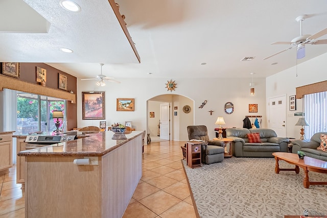 kitchen with stone counters, light tile patterned floors, a kitchen island, ceiling fan, and light brown cabinets