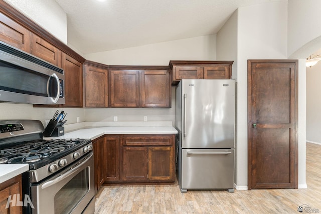 kitchen featuring light hardwood / wood-style flooring, vaulted ceiling, a textured ceiling, and appliances with stainless steel finishes