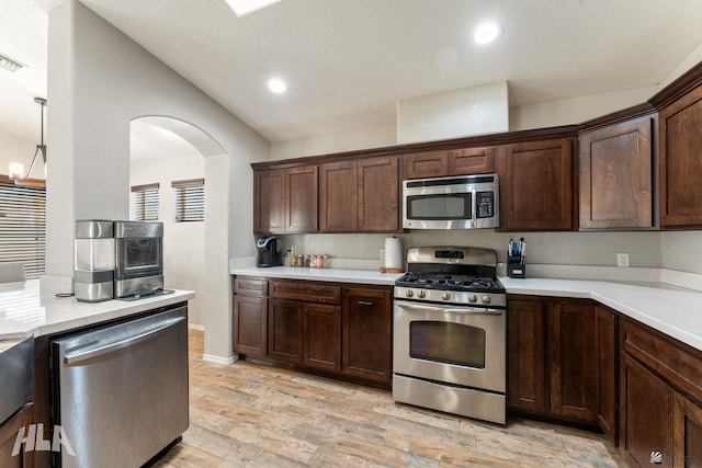 kitchen with lofted ceiling, appliances with stainless steel finishes, dark brown cabinets, and light wood-type flooring