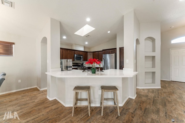 kitchen with appliances with stainless steel finishes, dark wood-type flooring, a breakfast bar area, and kitchen peninsula