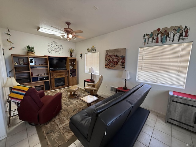 tiled living room with ceiling fan and a fireplace