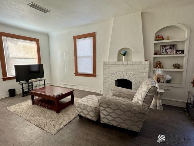 living room with built in shelves, a brick fireplace, a textured ceiling, and wood-type flooring