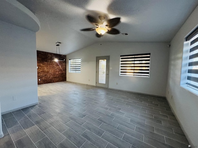 unfurnished living room with ceiling fan, brick wall, and vaulted ceiling