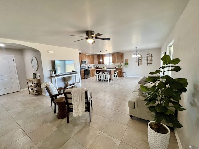 living room with ceiling fan with notable chandelier, light tile patterned floors, arched walkways, and baseboards