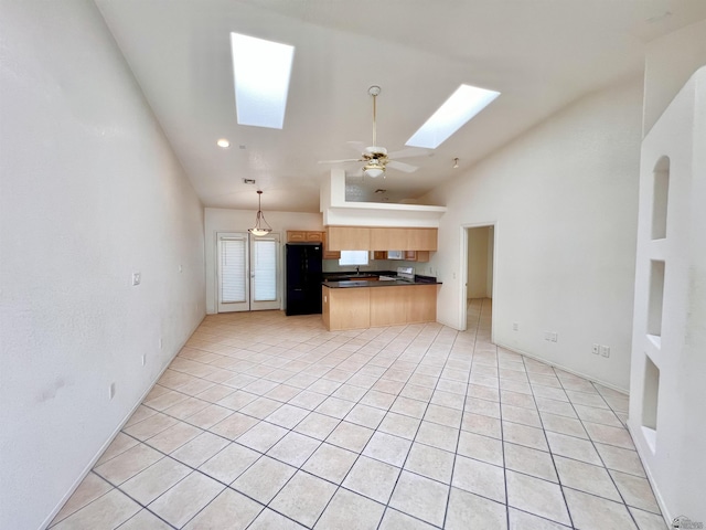 kitchen with black refrigerator, kitchen peninsula, a skylight, ceiling fan, and light tile patterned floors