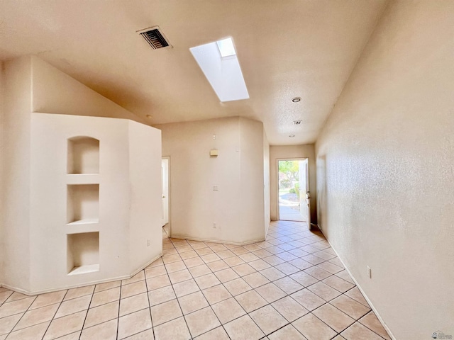 unfurnished room with a skylight, built in features, and light tile patterned floors