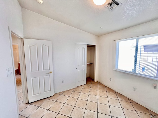 unfurnished bedroom with lofted ceiling, light tile patterned floors, a textured ceiling, and a closet