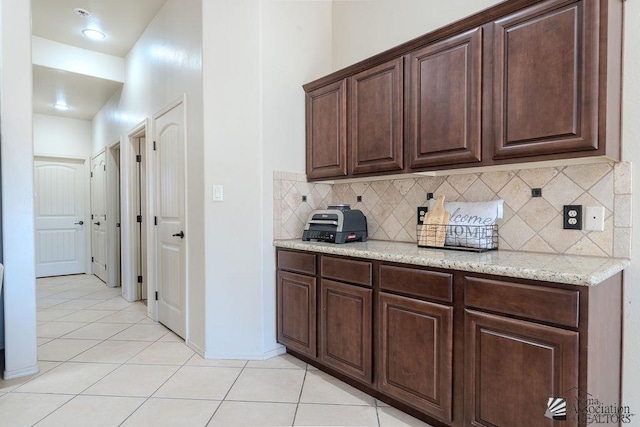 kitchen with light tile patterned floors, decorative backsplash, dark brown cabinets, light stone countertops, and baseboards