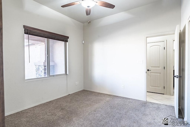 empty room featuring a ceiling fan, light carpet, and light tile patterned flooring