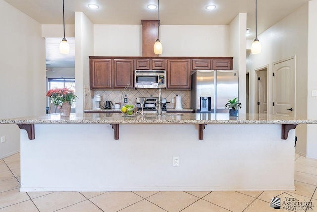 kitchen featuring light tile patterned floors, backsplash, appliances with stainless steel finishes, a sink, and a kitchen breakfast bar