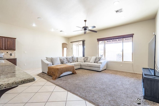 living area with light tile patterned floors, visible vents, arched walkways, a ceiling fan, and light colored carpet