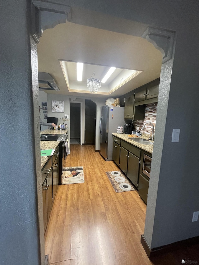 kitchen featuring sink, stainless steel refrigerator, a tray ceiling, light hardwood / wood-style floors, and wall chimney range hood