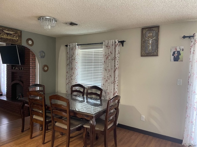 dining area with a brick fireplace, hardwood / wood-style floors, and a textured ceiling