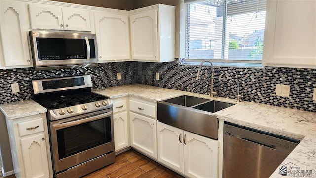 kitchen with tasteful backsplash, appliances with stainless steel finishes, white cabinets, and wood finished floors