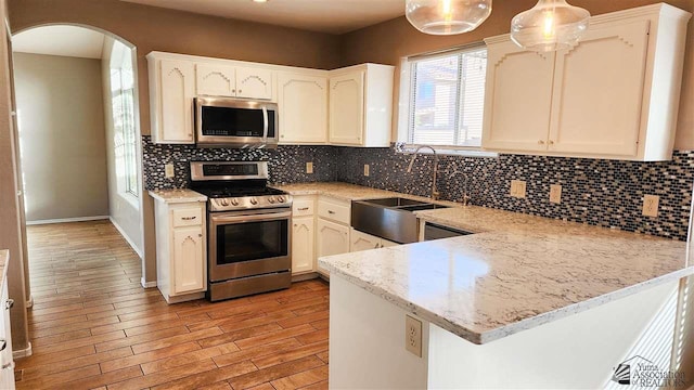 kitchen with arched walkways, stainless steel appliances, a peninsula, a sink, and decorative backsplash