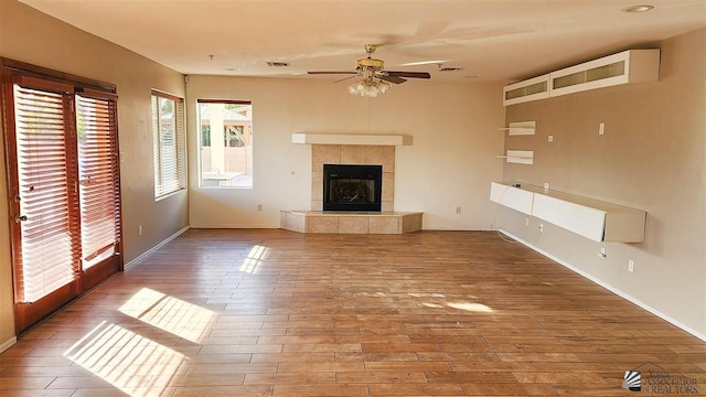 unfurnished living room featuring ceiling fan, a fireplace, baseboards, and wood finished floors