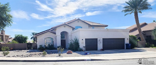 mediterranean / spanish house featuring stucco siding, fence, a garage, driveway, and a tiled roof