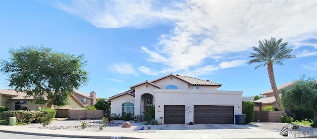 mediterranean / spanish house with a garage, concrete driveway, fence, and stucco siding