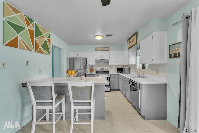 kitchen with light countertops, appliances with stainless steel finishes, white cabinetry, a peninsula, and a kitchen breakfast bar