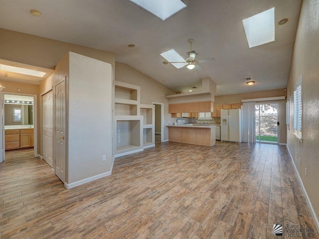 unfurnished living room featuring vaulted ceiling with skylight, light hardwood / wood-style flooring, ceiling fan, and built in shelves