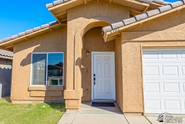 entrance to property with a garage, a tile roof, and stucco siding