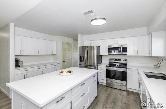 kitchen with stainless steel appliances, light countertops, visible vents, a sink, and wood finished floors