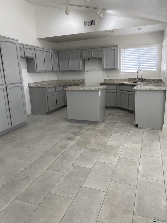 kitchen with gray cabinetry, sink, light tile patterned flooring, vaulted ceiling, and a kitchen island