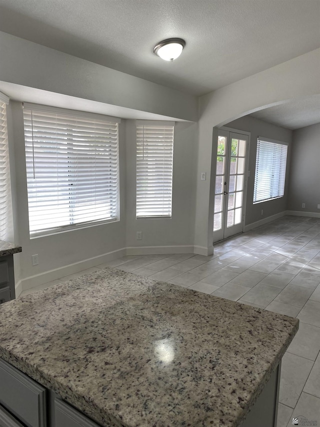 kitchen with light tile patterned flooring, light stone counters, a healthy amount of sunlight, and french doors