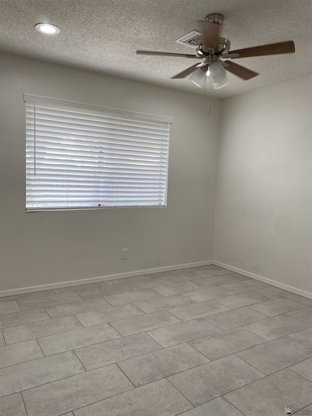 empty room with a textured ceiling, ceiling fan, and light tile patterned flooring