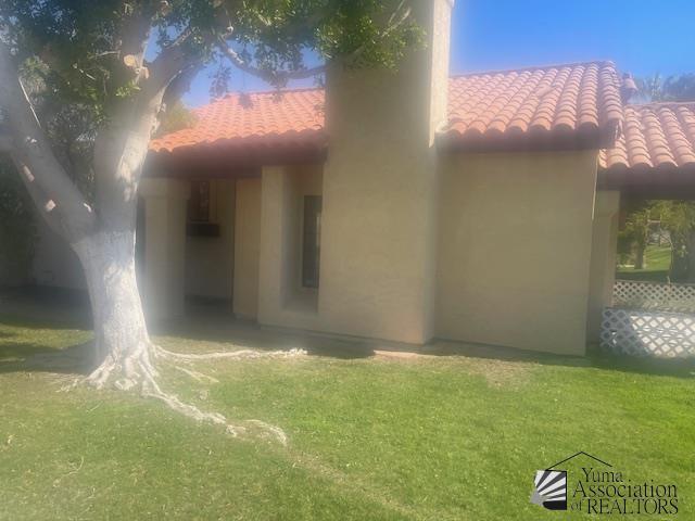 exterior space featuring a yard, a tiled roof, and stucco siding