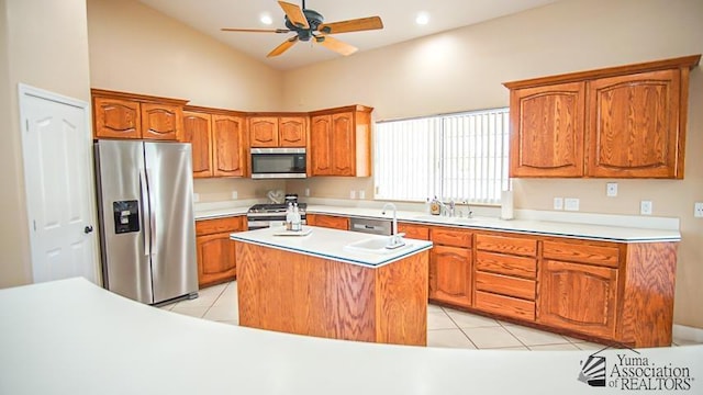 kitchen with a kitchen island, light tile patterned floors, brown cabinets, stainless steel appliances, and a sink