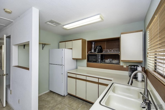 kitchen featuring sink, light tile patterned floors, white cabinets, and white refrigerator