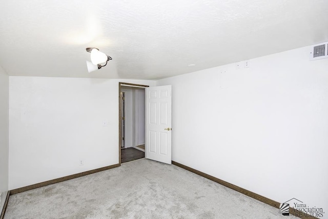 spare room featuring light colored carpet and a textured ceiling