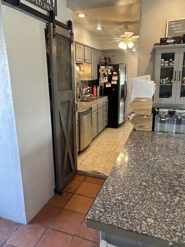 kitchen featuring stainless steel appliances, sink, gray cabinets, ceiling fan, and a barn door